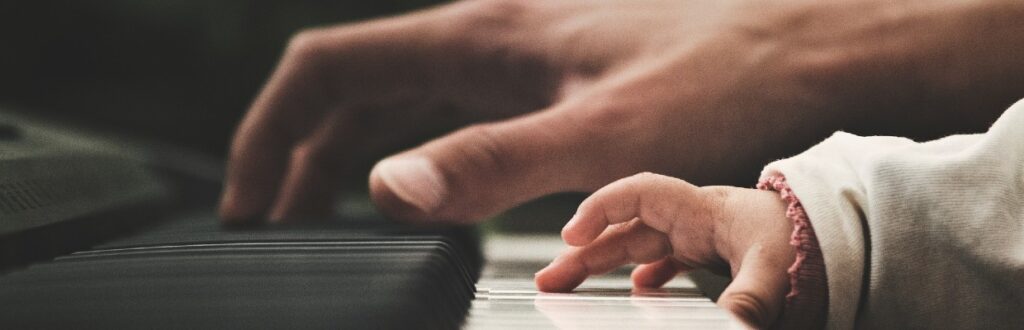 Piano, minkä koskettimilla näkyy aikuisen ja lapsen kädet